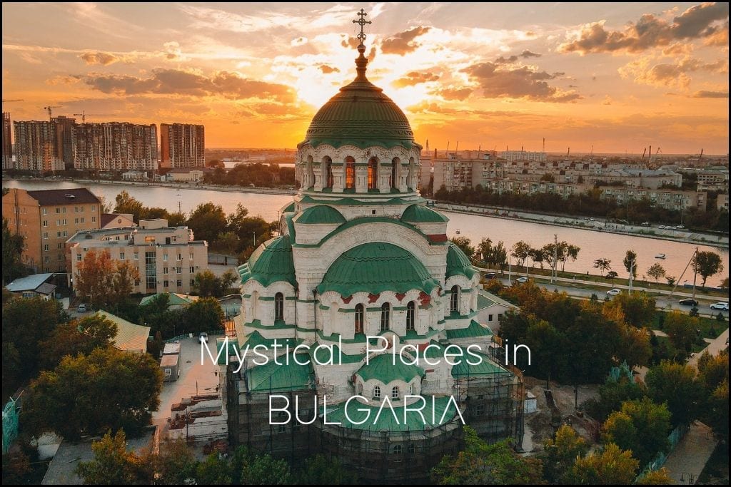 The Alexander Nevsky Cathedral in Sofia, Bulgaria, is captured at sunset with its domes shining against a backdrop of residential buildings and the sunset-kissed river. 'Mystical Places in BULGARIA' suggests the blog post will delve into the country's enchanting and spiritual locations.
