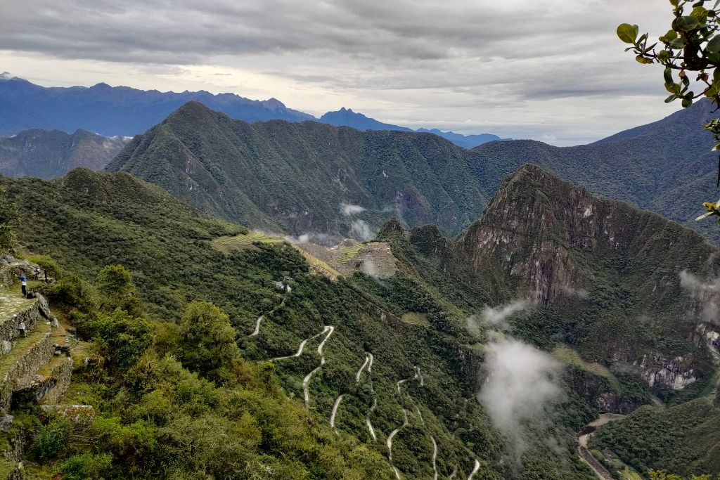 A breathtaking view of the Machu Picchu mountains enveloped by mist, with the ancient Incan ruins visible in the distance and a winding trail leading through the lush, verdant landscape.