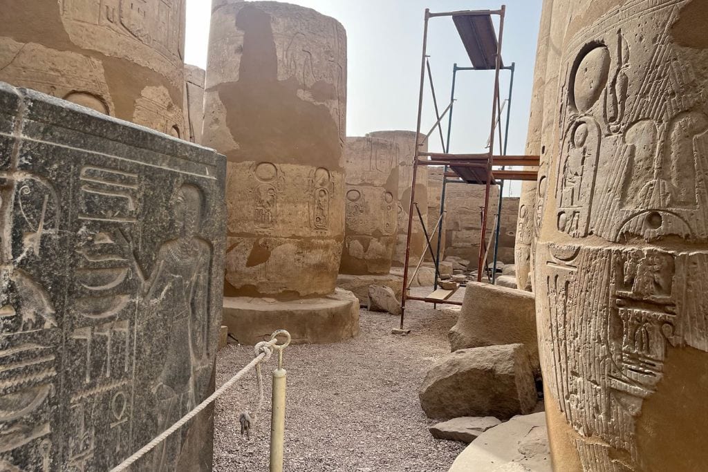 Luxor City in Egypt: Is it Worth Visiting? Inside the Medinet Habu Temple in Luxor, ancient columns and walls rich with hieroglyphs stand partially restored, with a wooden scaffolding hinting at ongoing archaeological preservation under a clear sky.