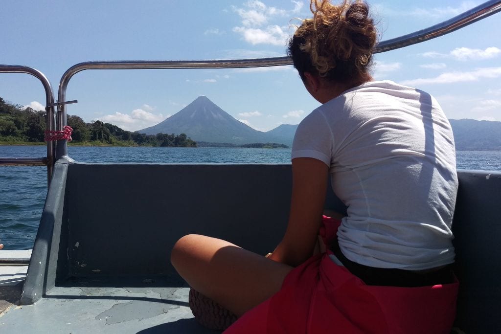 Arenal Volcano, Costa Rica: 2026 Spirituality Guide Passenger on a boat gazing at the Arenal Volcano in Costa Rica, a journey reflecting spirituality and connection with nature, with the volcano’s perfect cone shape dominating the landscape against a clear sky.