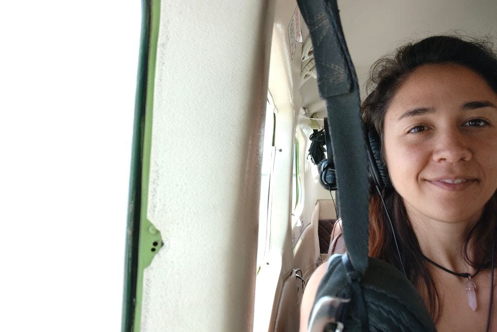 Why are the Lines of Nazca a Mystery of Peru? Woman with a content smile wearing headphones inside a small aircraft, with a window view partially showing, suggesting a flight over the enigmatic Lines of Nazca, one of the great mysteries of Peru.
