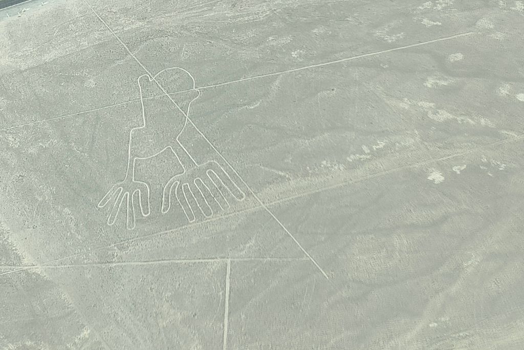 Why are the Lines of Nazca a Mystery of Peru? Aerial perspective of a section of the Nazca Lines featuring the figures of a tree and hands next to a roadway with nearby structures and vehicles, highlighting the interaction of ancient geoglyphs with modern infrastructure.