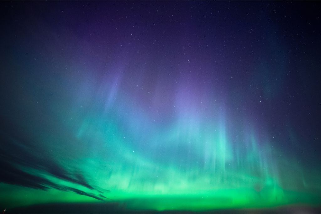 A stunning display of the Aurora Borealis with vivid green and purple lights cascading across the starlit night sky.