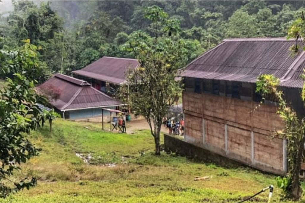 How to Get to the Lost City Colombia? My Personal Experience in 2026! A cluster of wooden buildings with metal roofs situated in a clearing, surrounded by lush vegetation and forested hills, serving as Camp 2 during the trek to the Lost City.