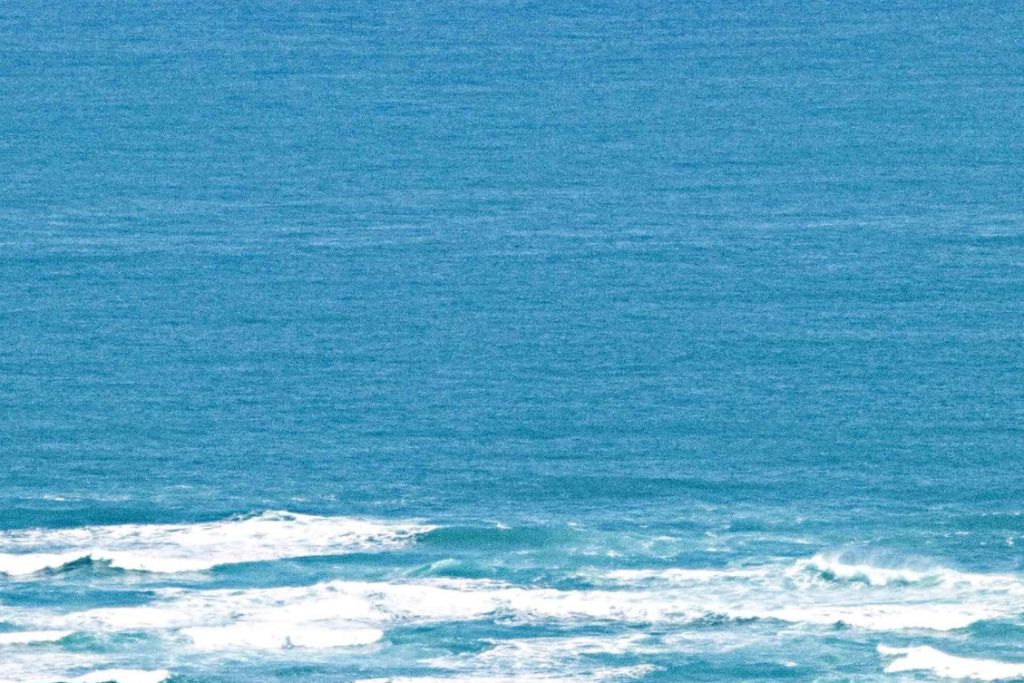 Cape Reinga: The Maori Sacred Site of New Zealand Wide shot of the blue ocean waters off Cape Reinga, with waves gently breaking along the coast, reflecting sunlight