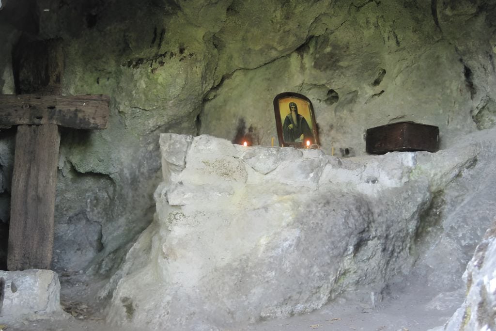 Rila Bulgaria Spiritual: The Most Spiritual Places to Visit in Bulgaria! The cave of St. John of Rila, featuring a simple altar with an icon of a saint, candles, and a wooden cross. The natural rock formations of the cave create a serene and spiritual atmosphere, reflecting the ascetic life of the hermit who once lived here.