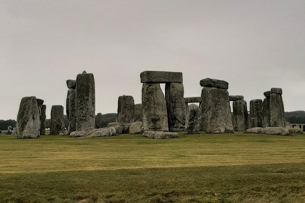 Best Way on How To Get To Stonehenge From London Wide view of Stonehenge with standing stones forming a circular structure against a cloudy sky and grassy landscape. How To Get To Stonehenge From London.