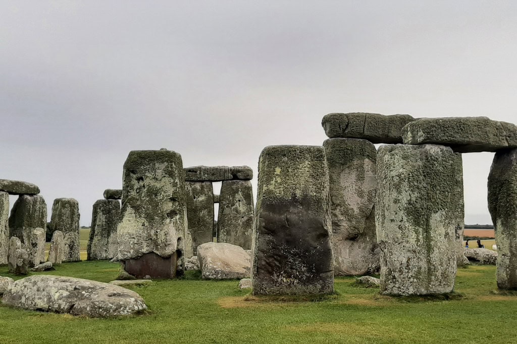 Best Way on How To Get To Stonehenge From London Close-up of Stonehenge, showing the ancient stone circle with massive weathered stones under a cloudy sky, surrounded by grass. How To Get To Stonehenge From London.