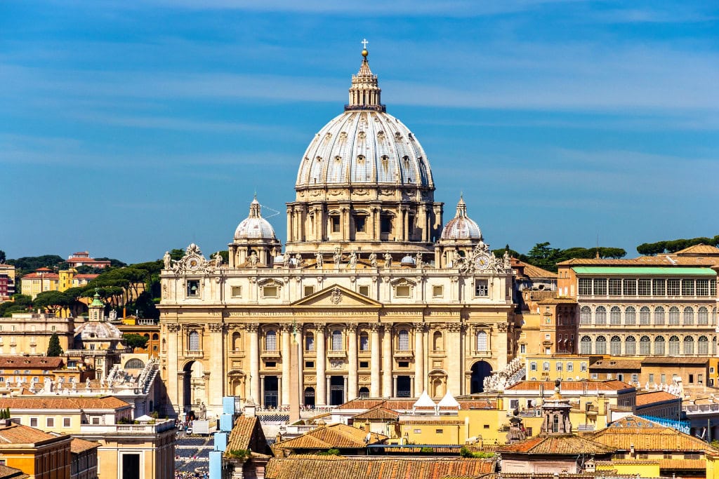 Spiritual Quest St. Peter Basilica (Vatican City) St. Peter's Basilica in Vatican City, showcasing its grand dome and ornate architecture under a clear blue sky, surrounded by the rooftops of Rome.