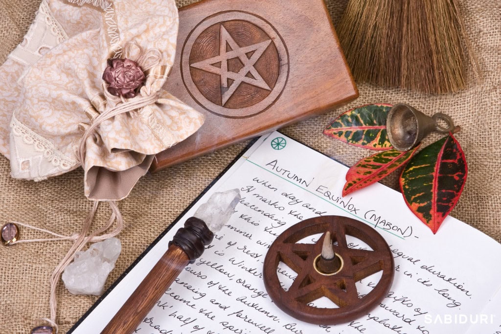 A Mabon altar setup honoring the Celtic Wheel, featuring a handwritten journal entry titled 'Autumn Equinox (Mabon),' a wooden pentacle box, a ritual wand with a crystal tip, and autumn leaves. Surrounding elements include a small brass bell, a burlap pouch with a decorative seal, and a wooden incense holder carved with a pentagram. This sacred arrangement symbolizes balance, gratitude, and the transition into the darker half of the year.