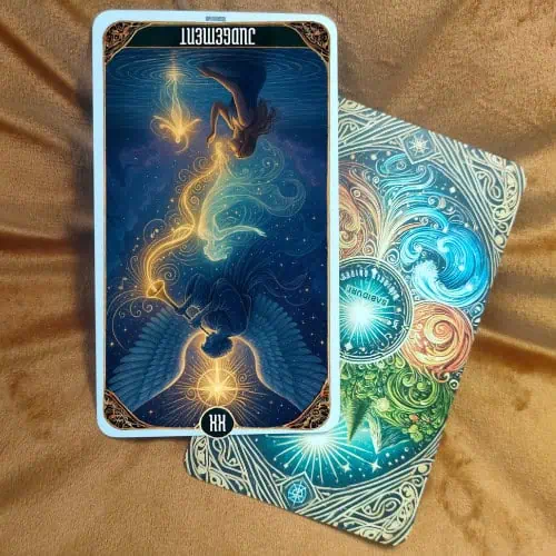 The Judgement Tarot Card reversed version showing the same angel with large wings and trumpet, but positioned upside down. The divine light, celestial symbols, clouds, and figures rising from the water are still present but inverted, symbolizing the reversed meaning of the card.