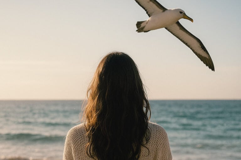 A woman standing on the beach at sunset, looking toward the ocean as an albatross flies overhead, symbolizing guidance from the albatross spirit animal.