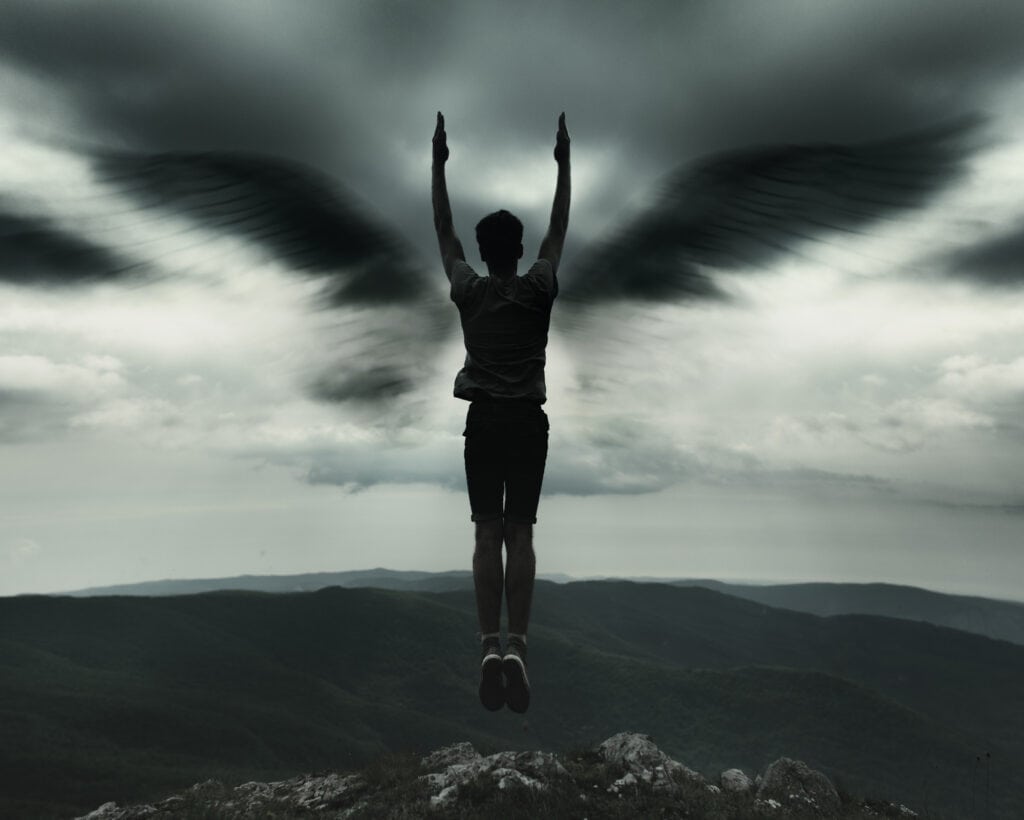 Why You Keep Seeing Angel Number 2 Everywhere A person standing on a mountain with raised arms, dark angel wings extending against a stormy sky. Evokes the transformative energy and duality reflected in Angel Number 2.