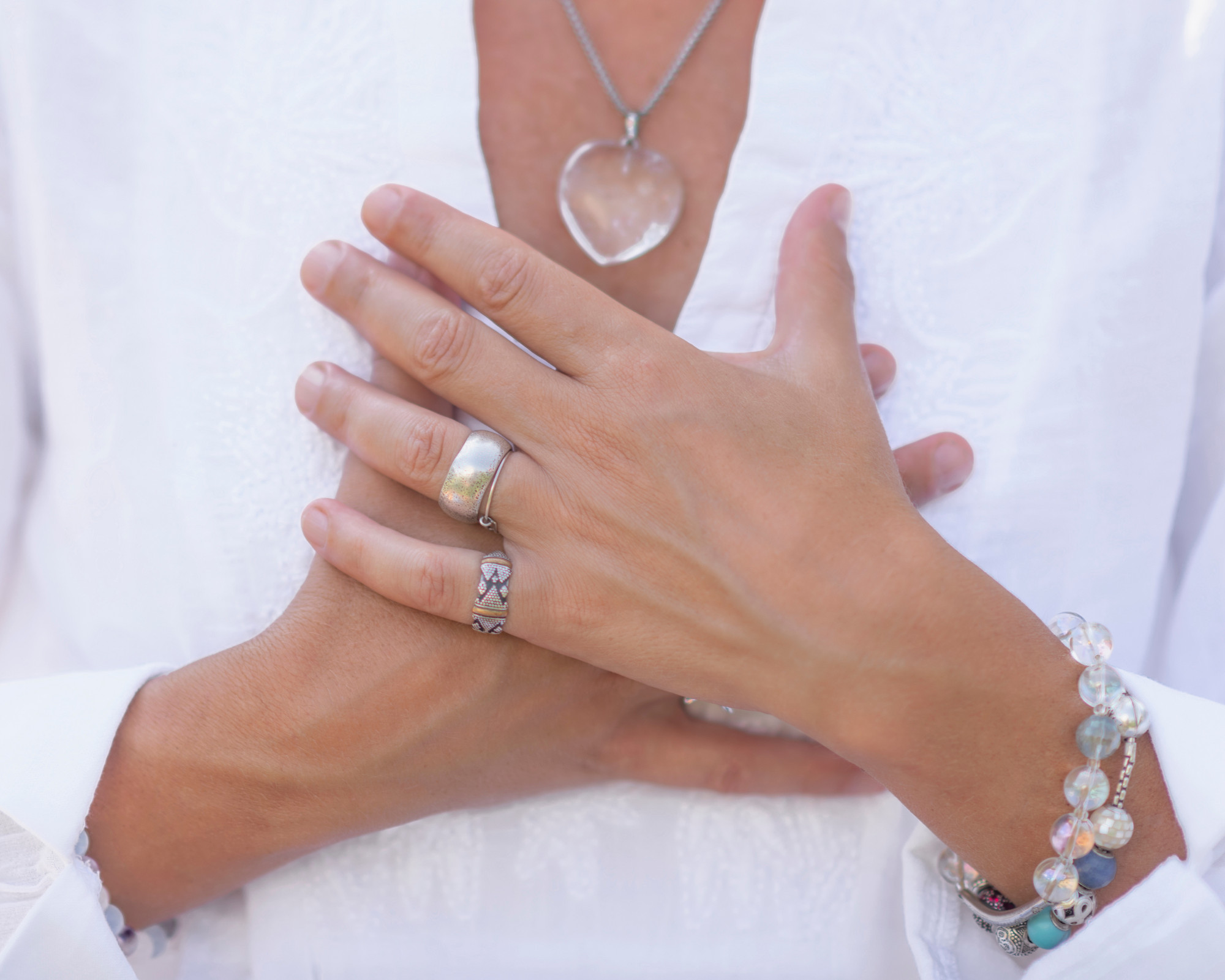 Anahata Chakra Meaning: All About the Heart Chakra Powers Person placing both hands over their heart while wearing a clear quartz heart necklace, symbolizing emotional healing and heart chakra activation.
