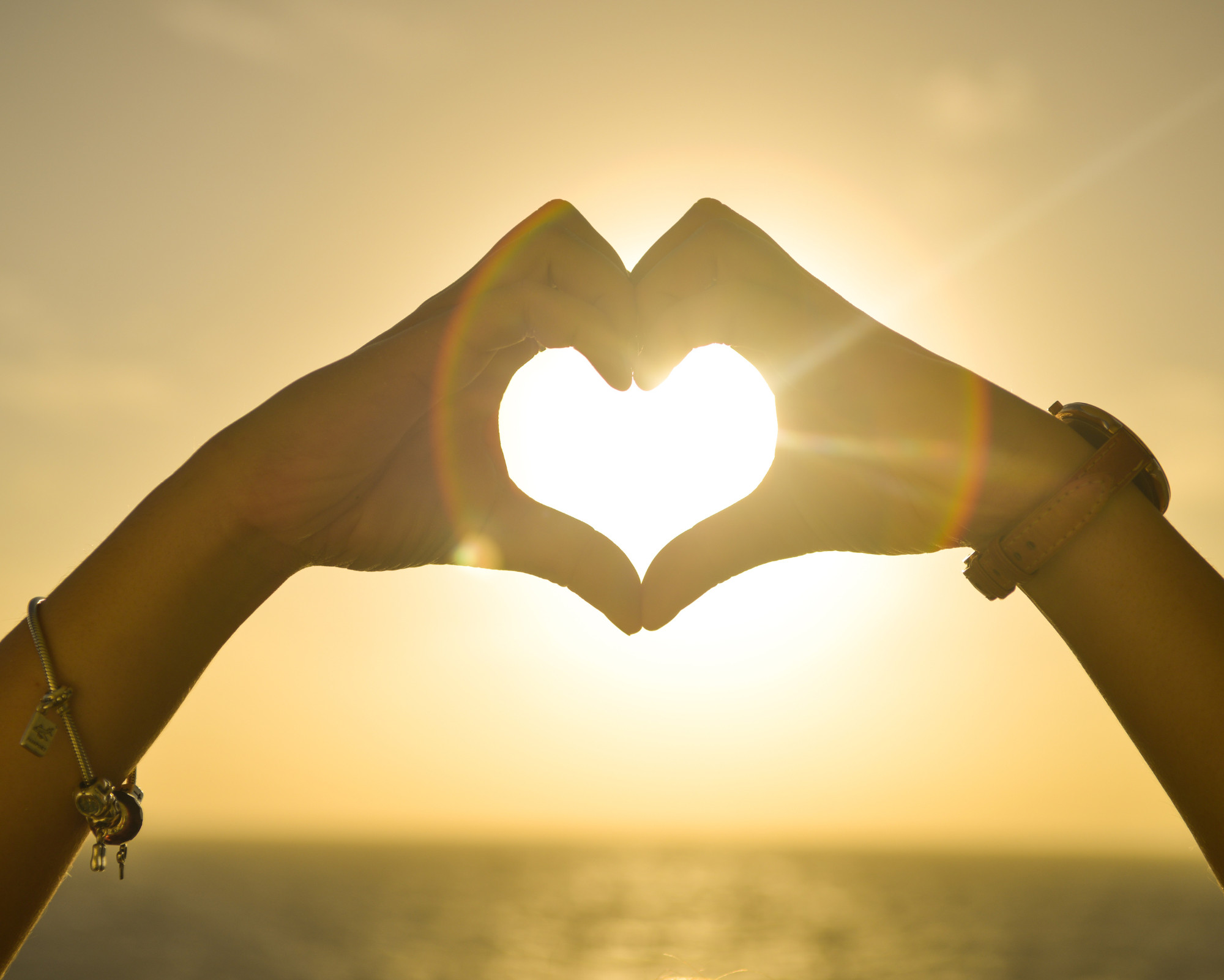 Anahata Chakra Meaning: All About the Heart Chakra Powers Hands forming a heart shape in front of the sun during a golden sunset, symbolizing love, connection, and heart chakra energy.
