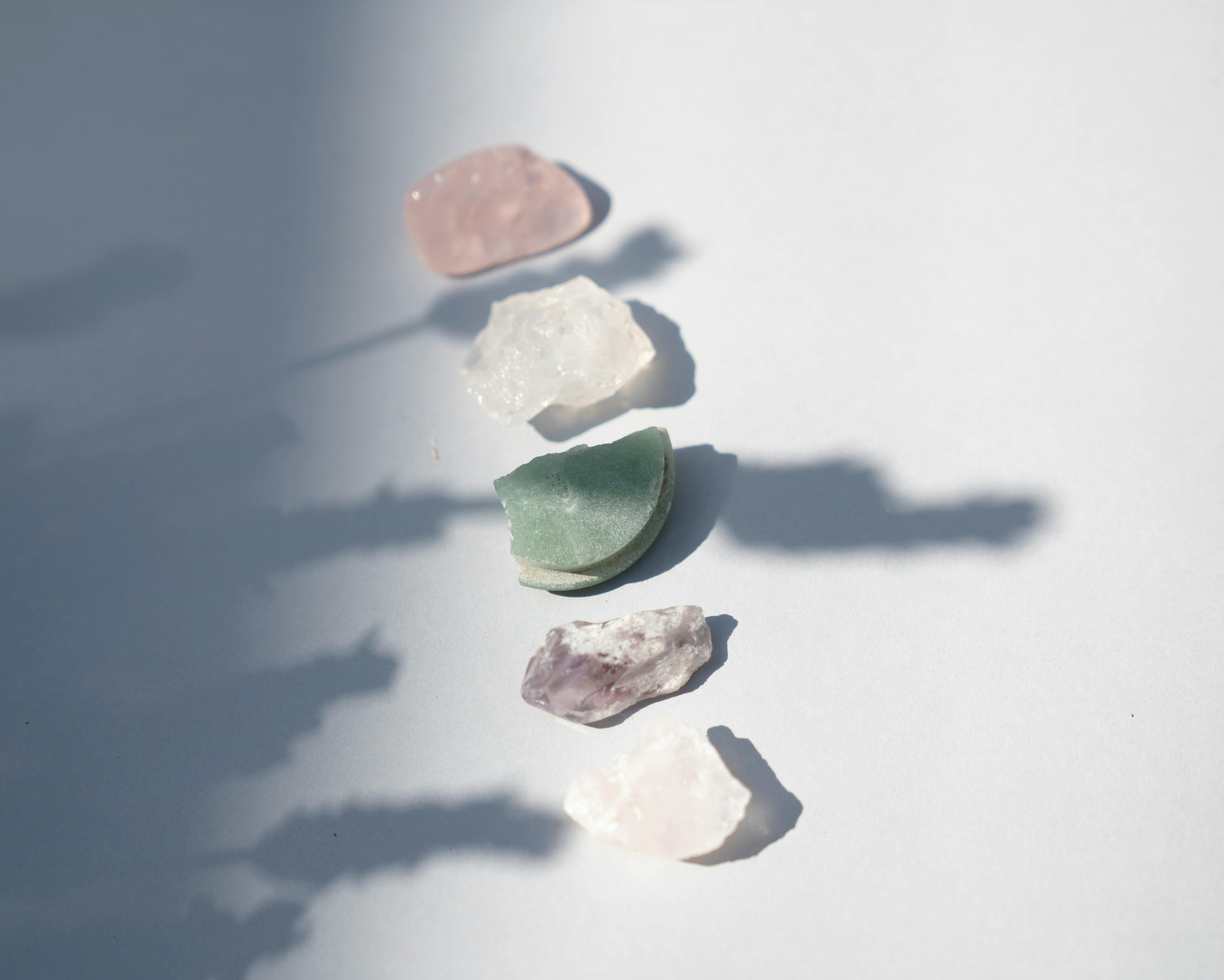 Anahata Chakra Meaning: All About the Heart Chakra Powers Various heart chakra crystals, including rose quartz, green aventurine, and amethyst, arranged on a white surface in natural sunlight.