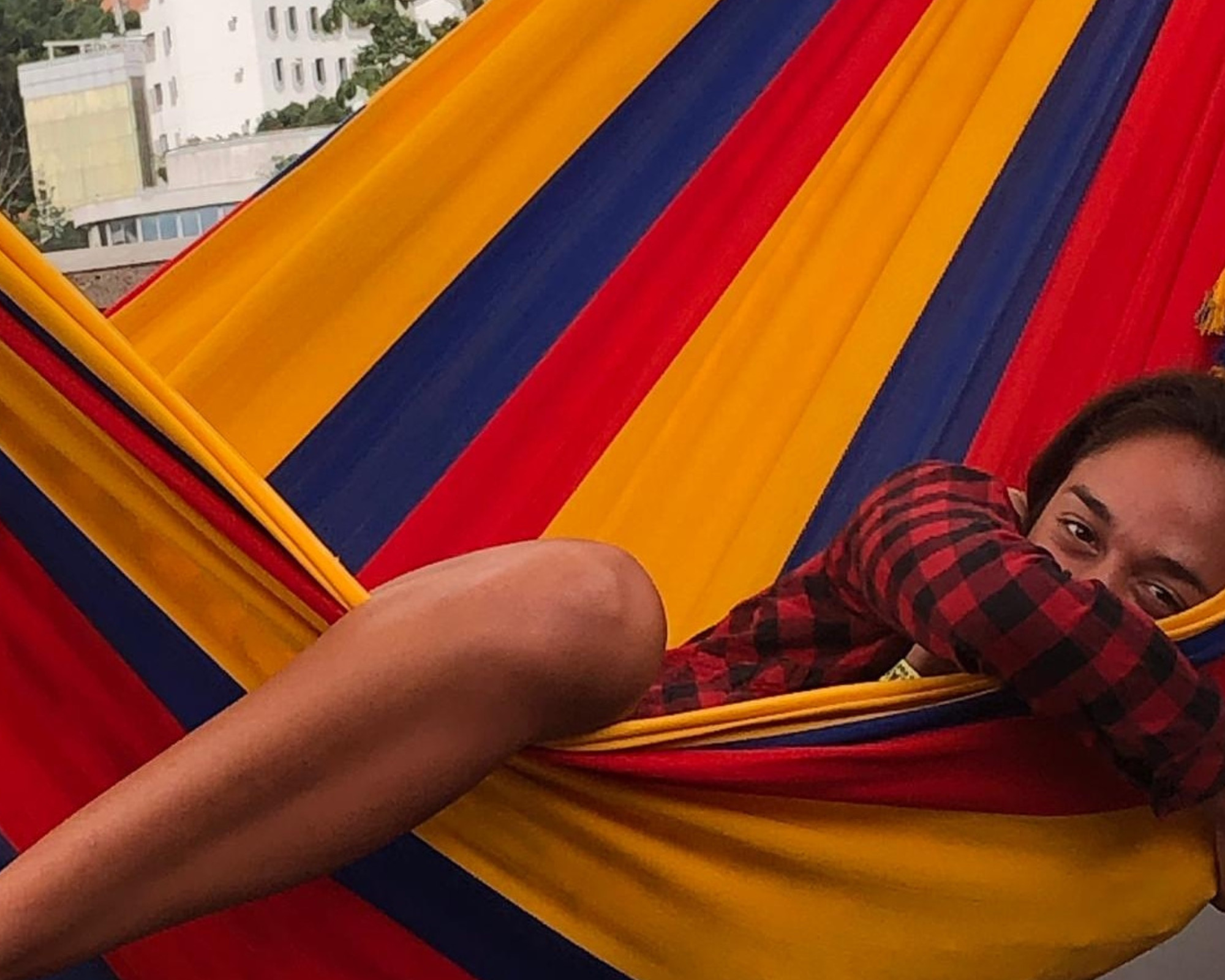 Person resting in a vibrant red, yellow, and blue hammock on a balcony, smiling peacefully while relaxing outdoors.