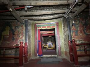 The Silence Between the Monasteries: What Spiti Valley Taught Me About Stillness Dimly lit interior corridor of Tabo Monastery with ancient wall murals, wooden beams overhead, and a doorway leading to a small shrine room.