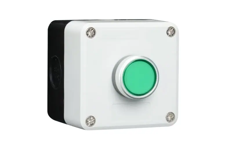 Emergency stop button, industrial safety control, white plastic housing with green alert button, mounted on wall for safety procedures.