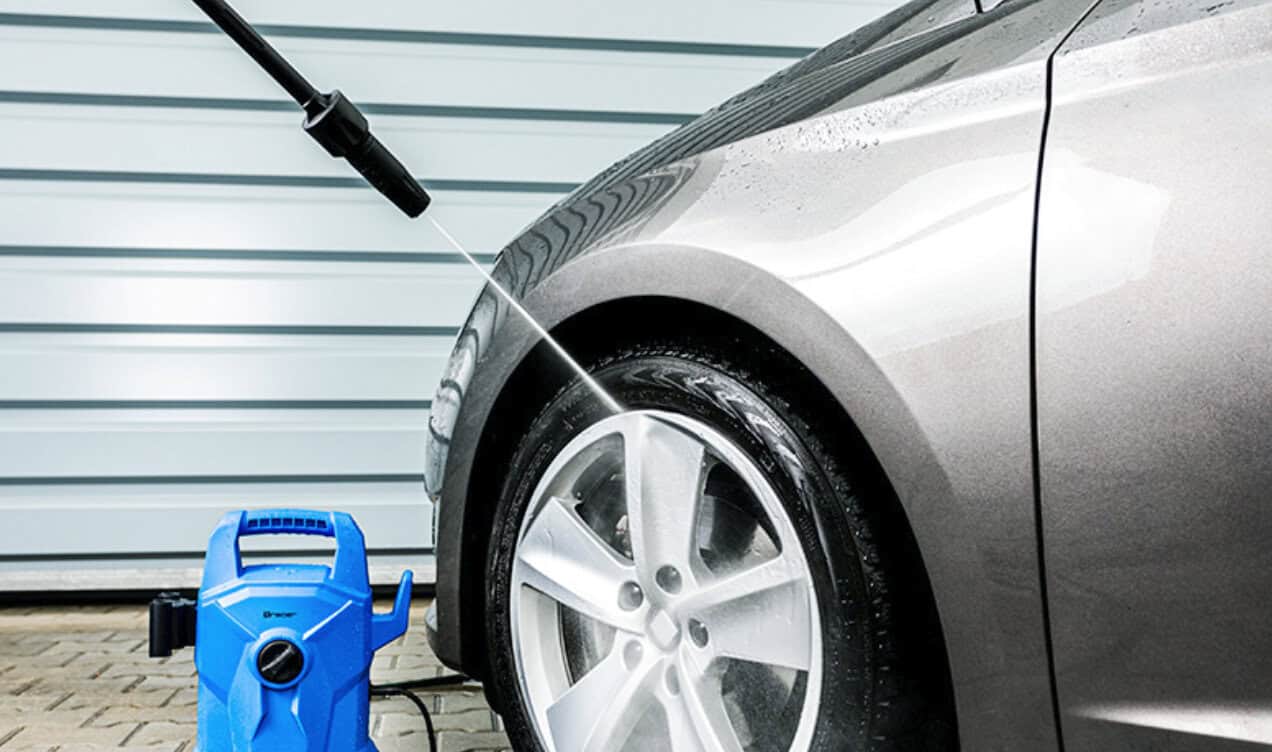 High-pressure car washer cleaning a gray vehicle with a blue pressure washer machine, outdoor setting, effective for vehicle maintenance and detailing.