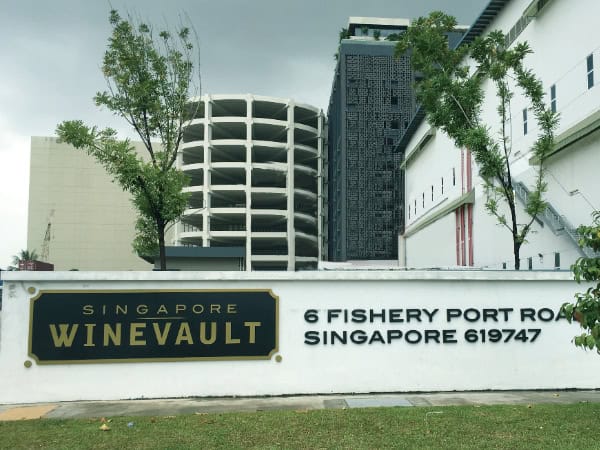 1. Large modern commercial buildings with security fences at Singapore WineVault on Fishery Port Road, featuring green trees and a clear sky.