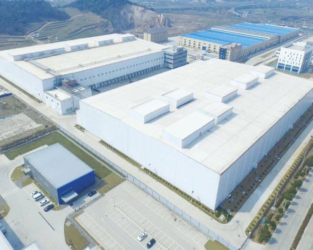 Aerial view of Safeguard Systems Group manufacturing facility in China, showcasing large industrial warehouses with extensive parking areas and surrounding landscape.