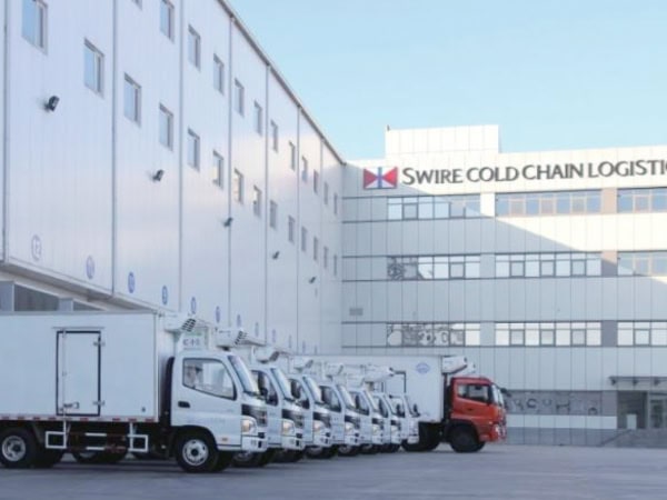 Semi-trucks parked outside a large logistics warehouse with "Swire Cold Chain Logistics" signage.