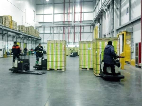 Efficient warehouse workers using forklifts to transport stacked boxes in a modern, well-lit distribution center.