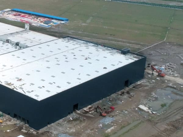 Large industrial warehouse under construction with a white roof and black exterior walls, surrounded by construction equipment and unfinished ground, representing Safeguard Systems Group's manufacturing facilities in China.