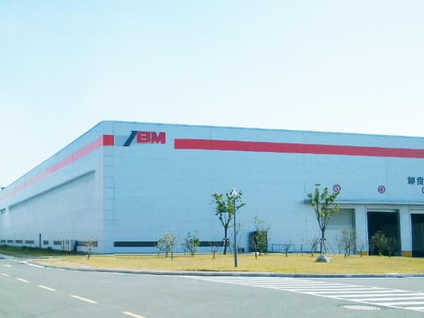 1. Modern industrial warehouse building with SBM logo, surrounded by a clean parking area and green trees, representing a large manufacturing presence in China.