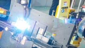 High-tech welding process with bright sparks and robotic machinery in an industrial manufacturing setting, showcasing advanced automation and safety equipment.