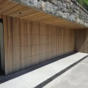 Bespoke batten garage door installed under a natural stone wall showcasing premium vertical timber slatted design profiles for modern homes