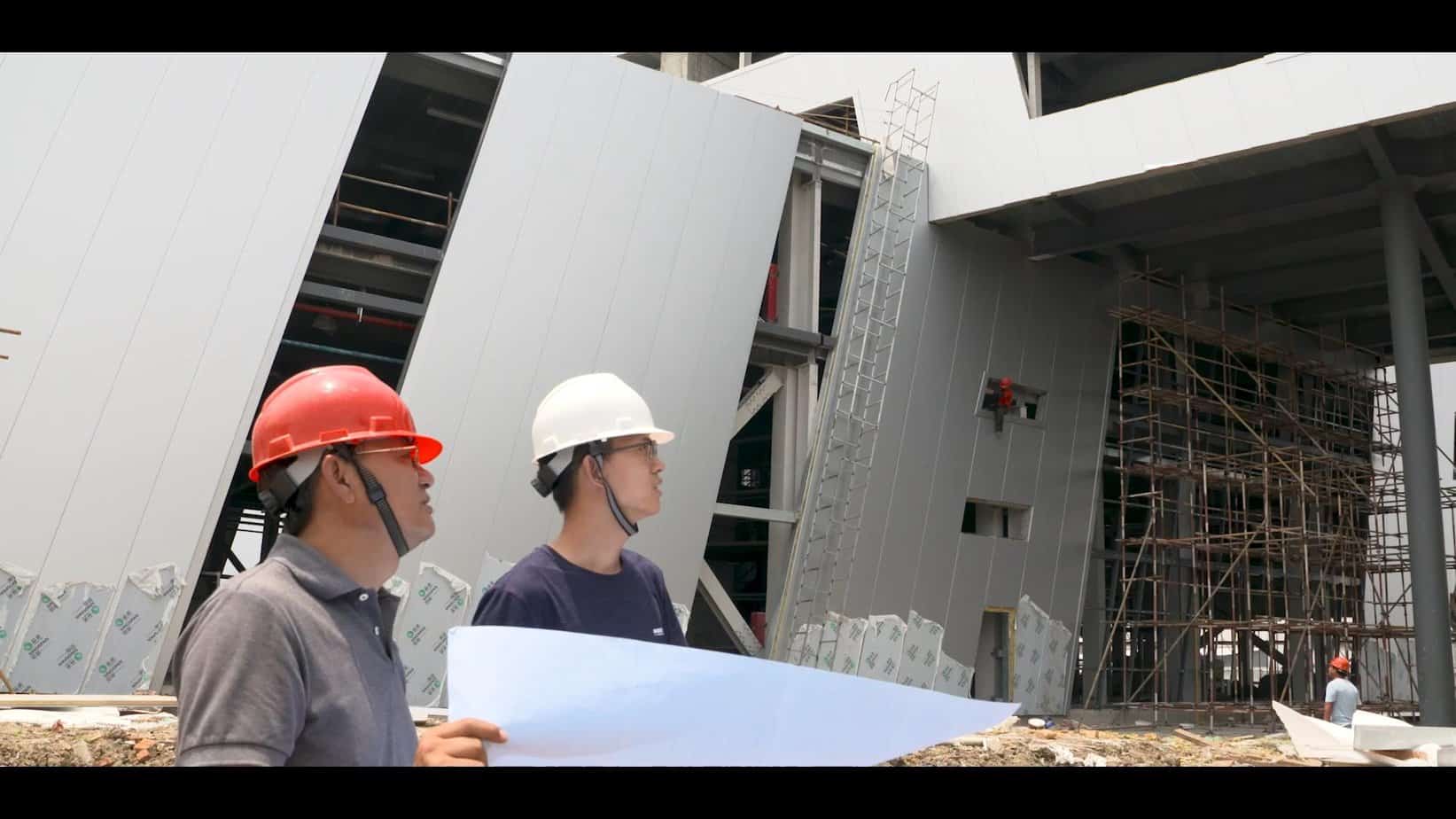 High-rise construction site with workers wearing safety helmets and inspecting blueprints, showcasing modern building development and scaffolding safety measures.