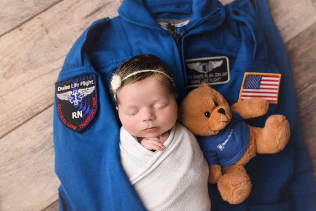 Newborn Baby Girl with teddybear laying on Daddys life flight suit