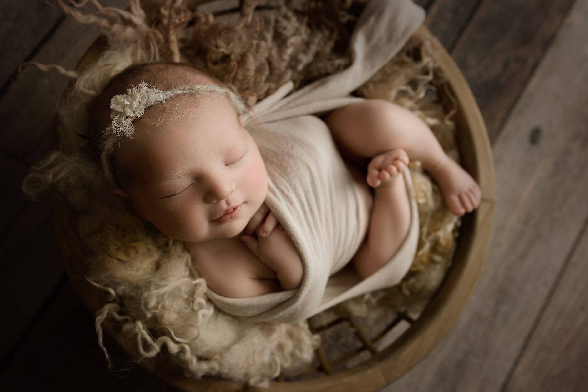 ### Newborn baby girl wrapped in beige in a wooden bowl