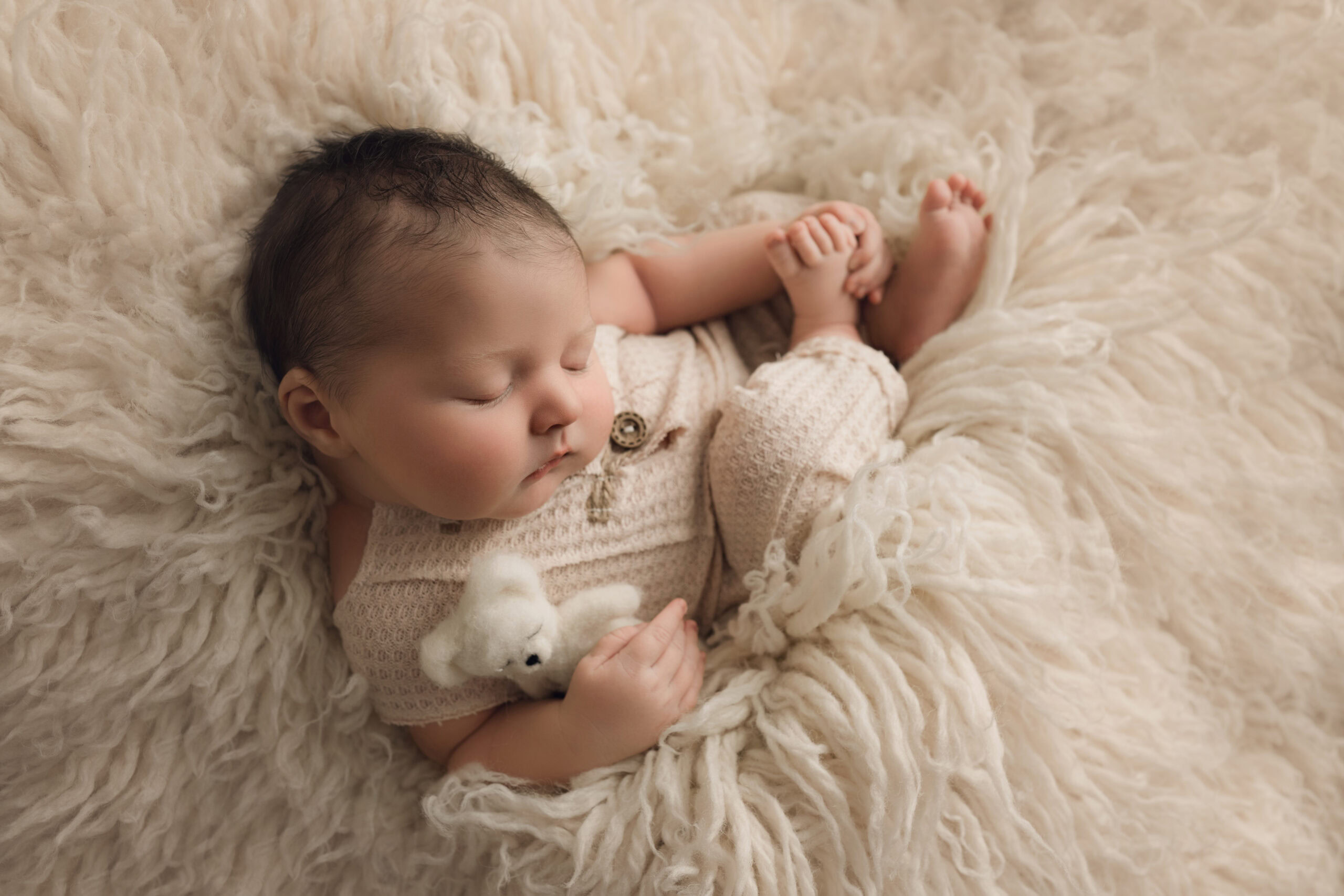 ### Newborn baby boy sleeping curled up with a teddy bear on white fur