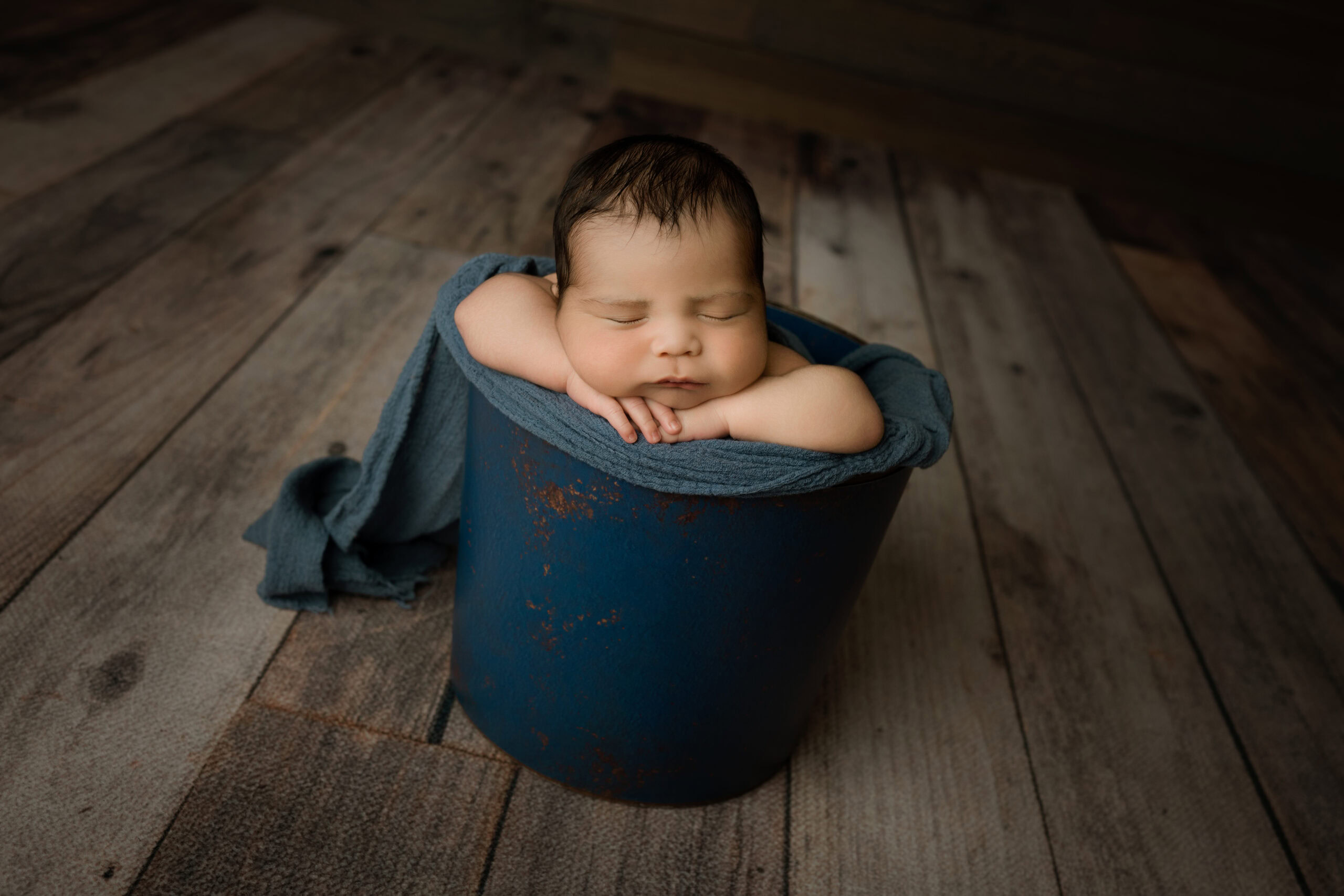 newborn baby boy sleeping in a blue bucket face up
