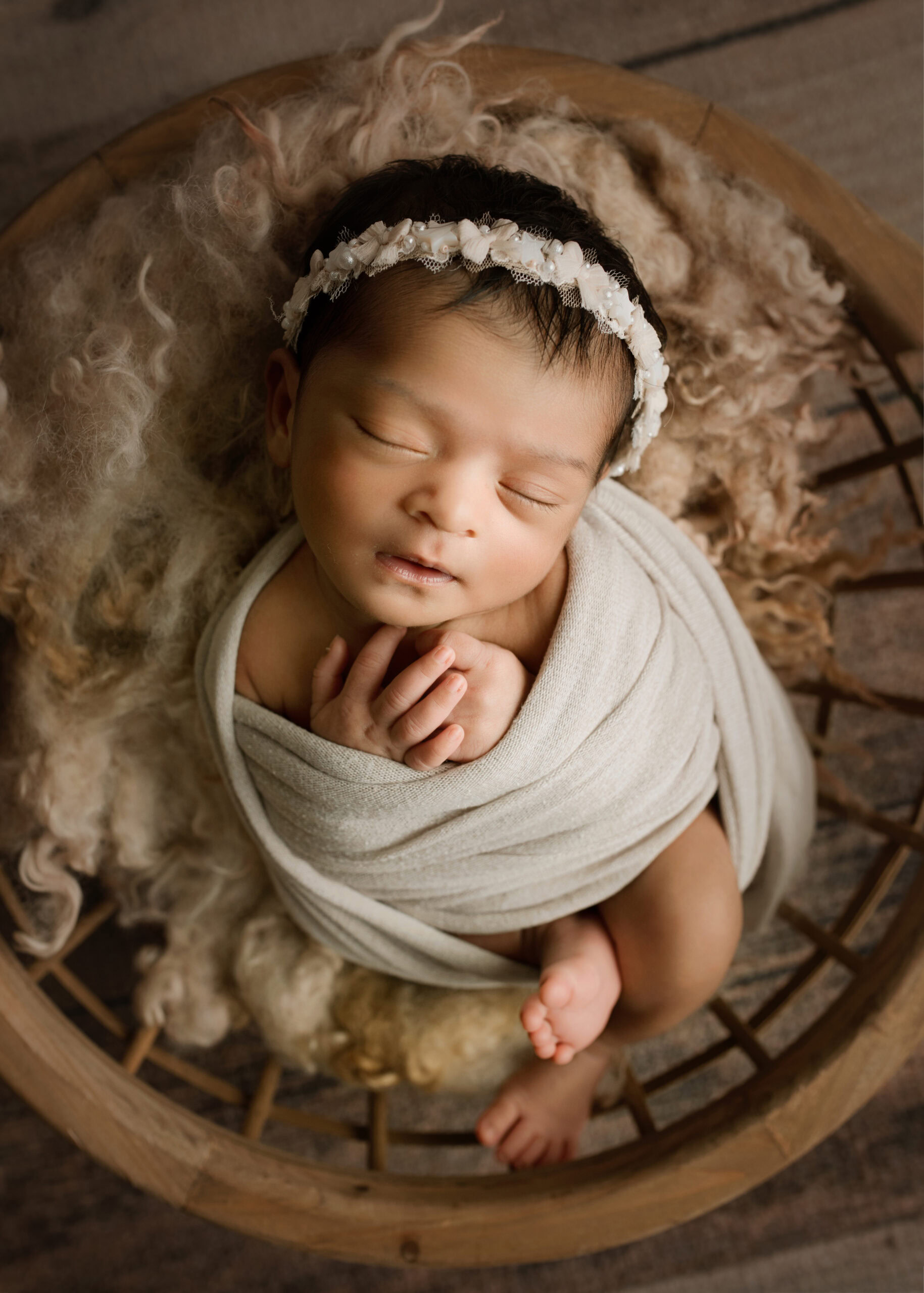 Newborn Baby Girl wrapped in a cream wrap with a pearl headband in a bowl