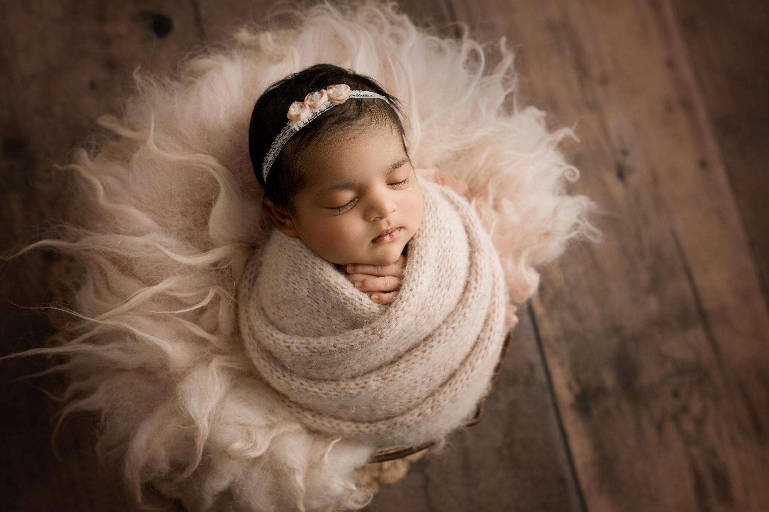 Newborn Baby Girl wrapped in a pink knit wrap and matching bow sleeping in a bucket of pink fur