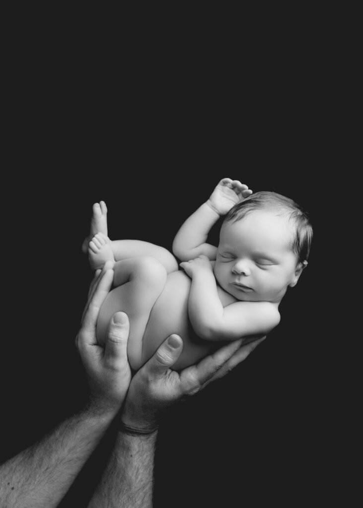 A black and white family portrait session with a newborn baby in daddy's hands