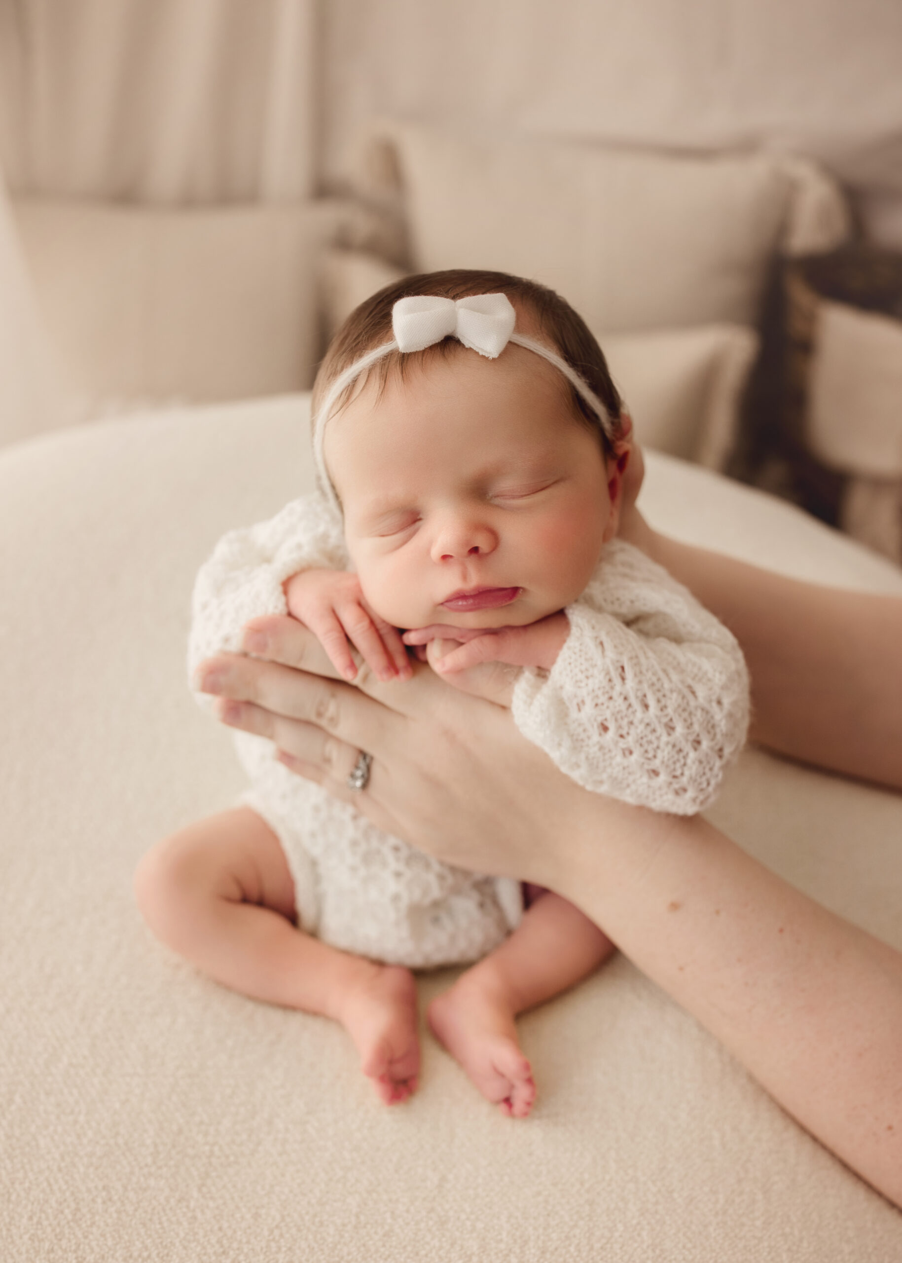 A newborn girl is sleeping in a white outfit sitting in mommy's hands.