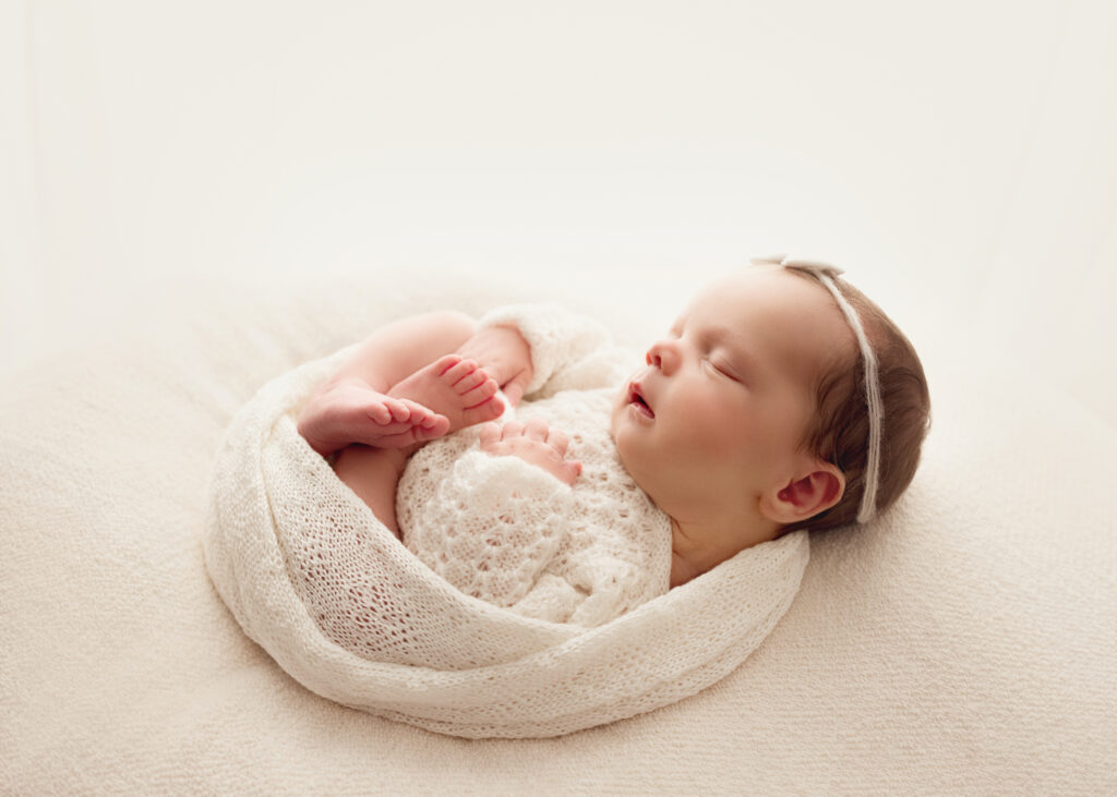 A newborn girl is curled up sleeping in a white wrap. Raleigh Newborn Photographer
