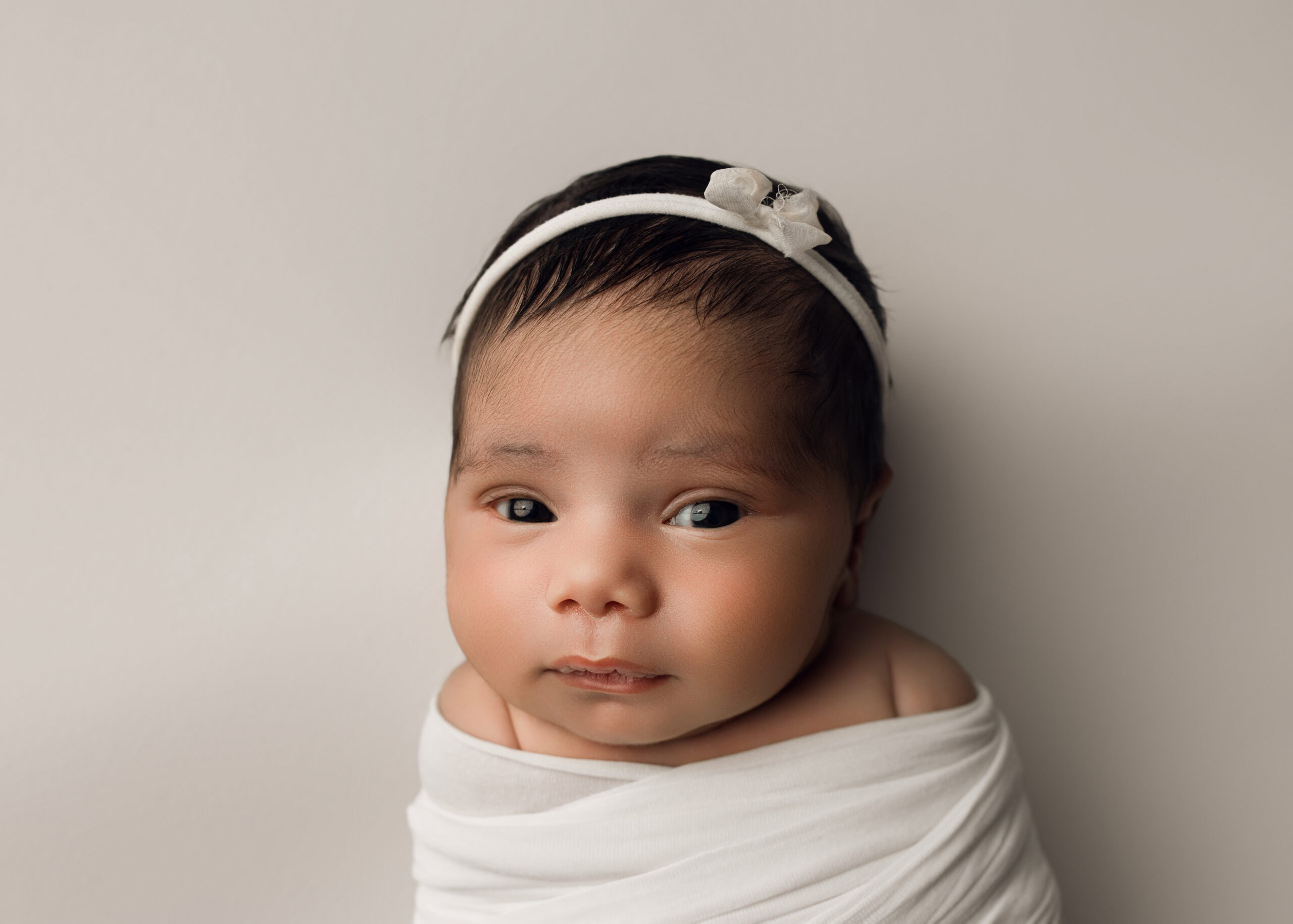Newborn baby girl wrapped in a white wrap and matching bow on a white background