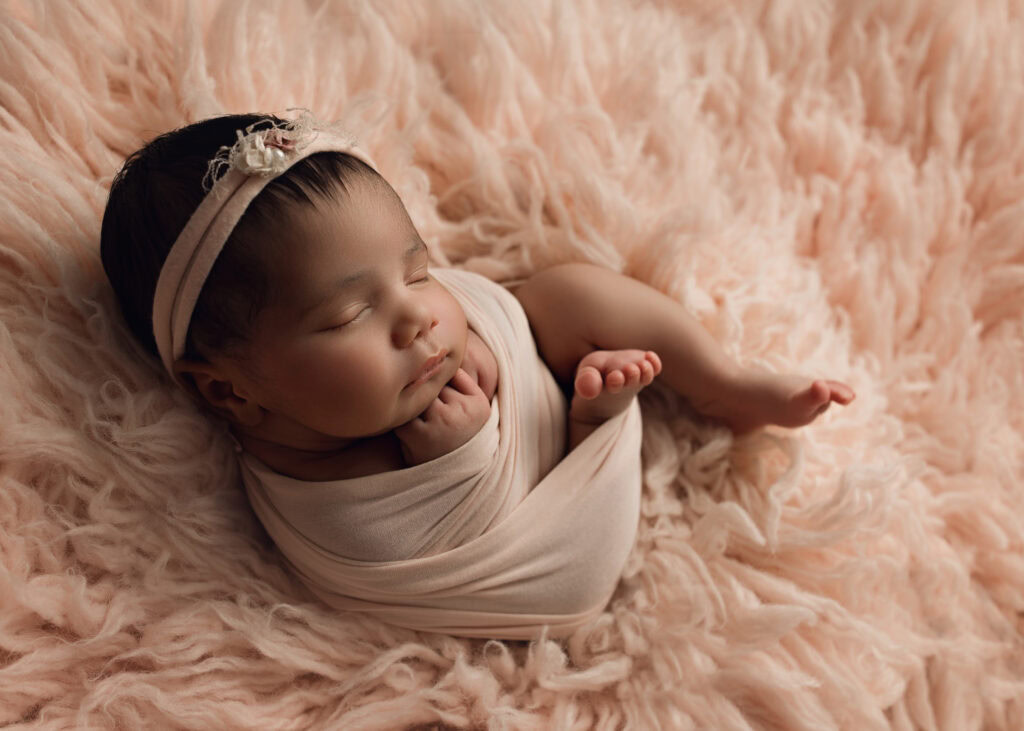 Raleigh Newborn baby girl wrapped in a pink wrap and matching bow on blush pink fur