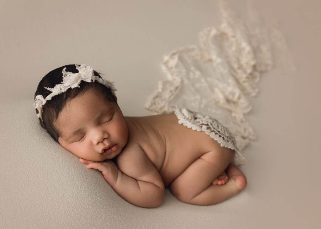 Newborn baby girl bum up with a cream bow and matching lace cover