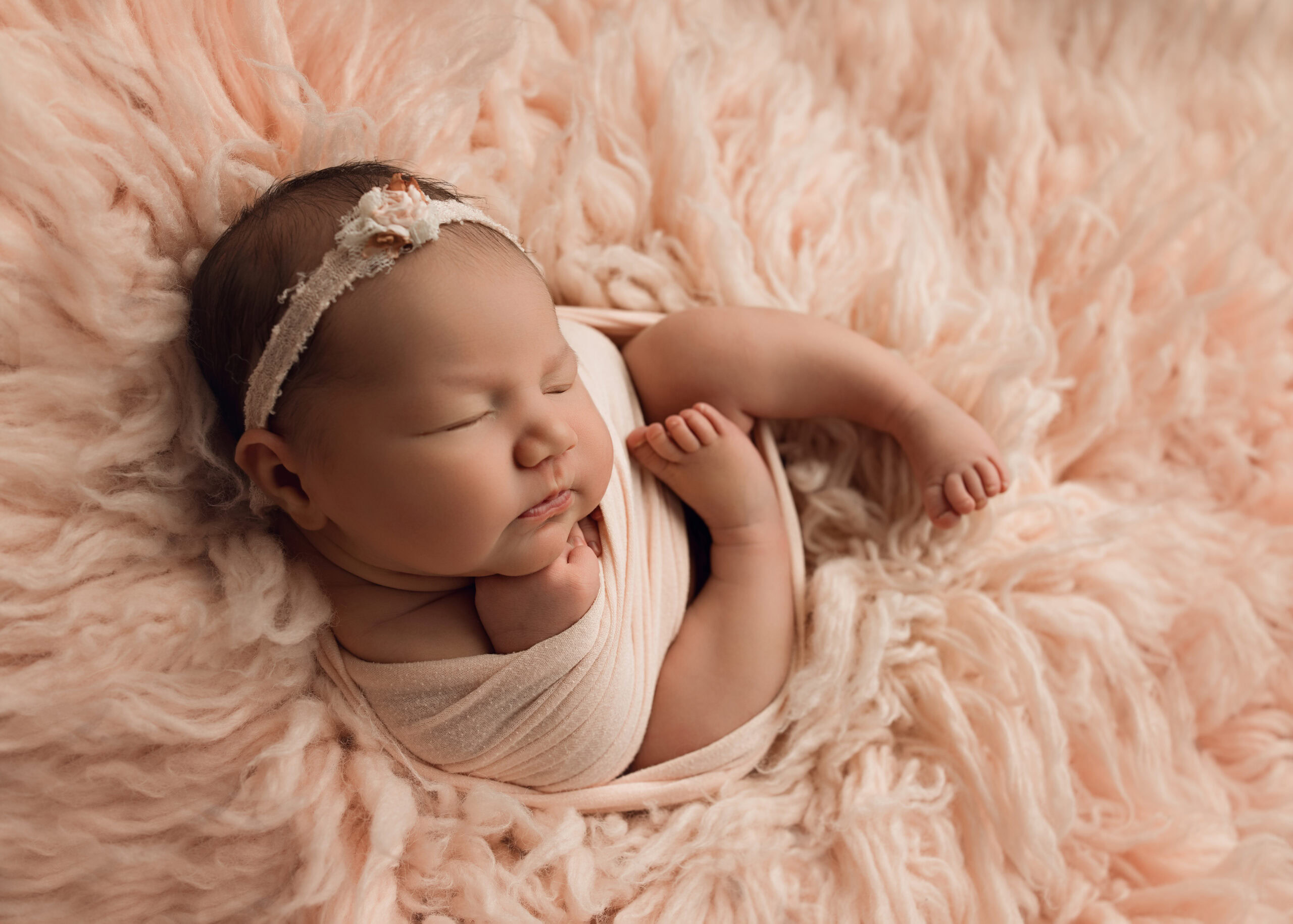 Newborn baby girl sleeping curled up in a pink wrap on pink fur