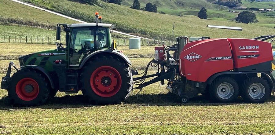 Tractor with hay baling equipment working on New Zealand farmland.