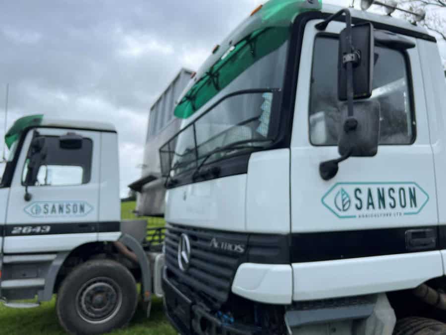 Modern Sanson Agriculture trucks parked on green fields in New Zealand.