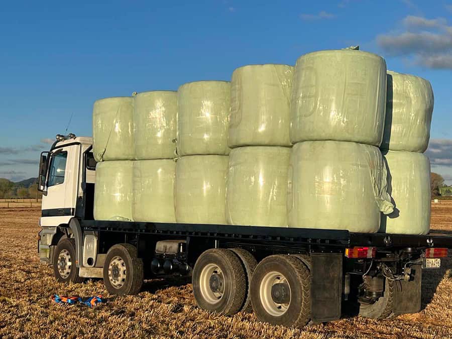 Bulk hay bales on flatbed truck in rural farmland, New Zealand.