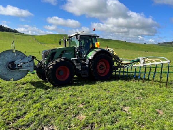 Sanson Agriculture tractor spraying pasture with a boom sprayer on lush New Zealand farmland.